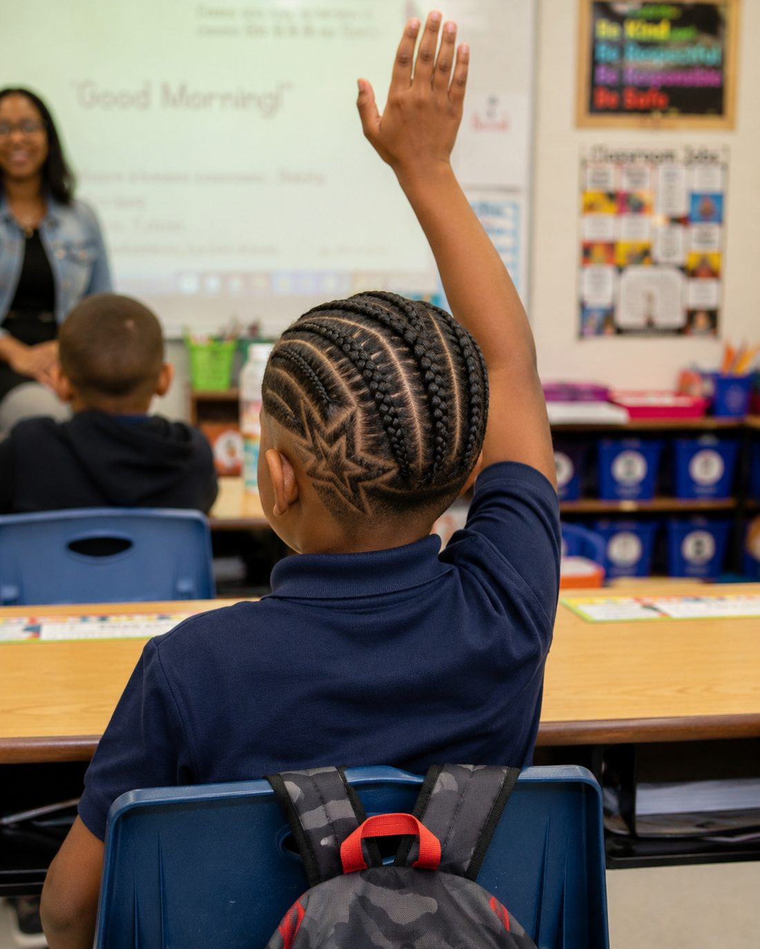 Young boy with star-design cornrows raising his hand proudly in class